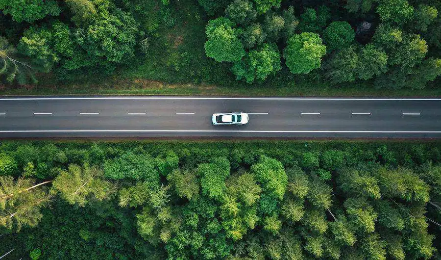 Electric car on open highway surrounded by trees, representing EV range anxiety and regional driving in Perth WA
