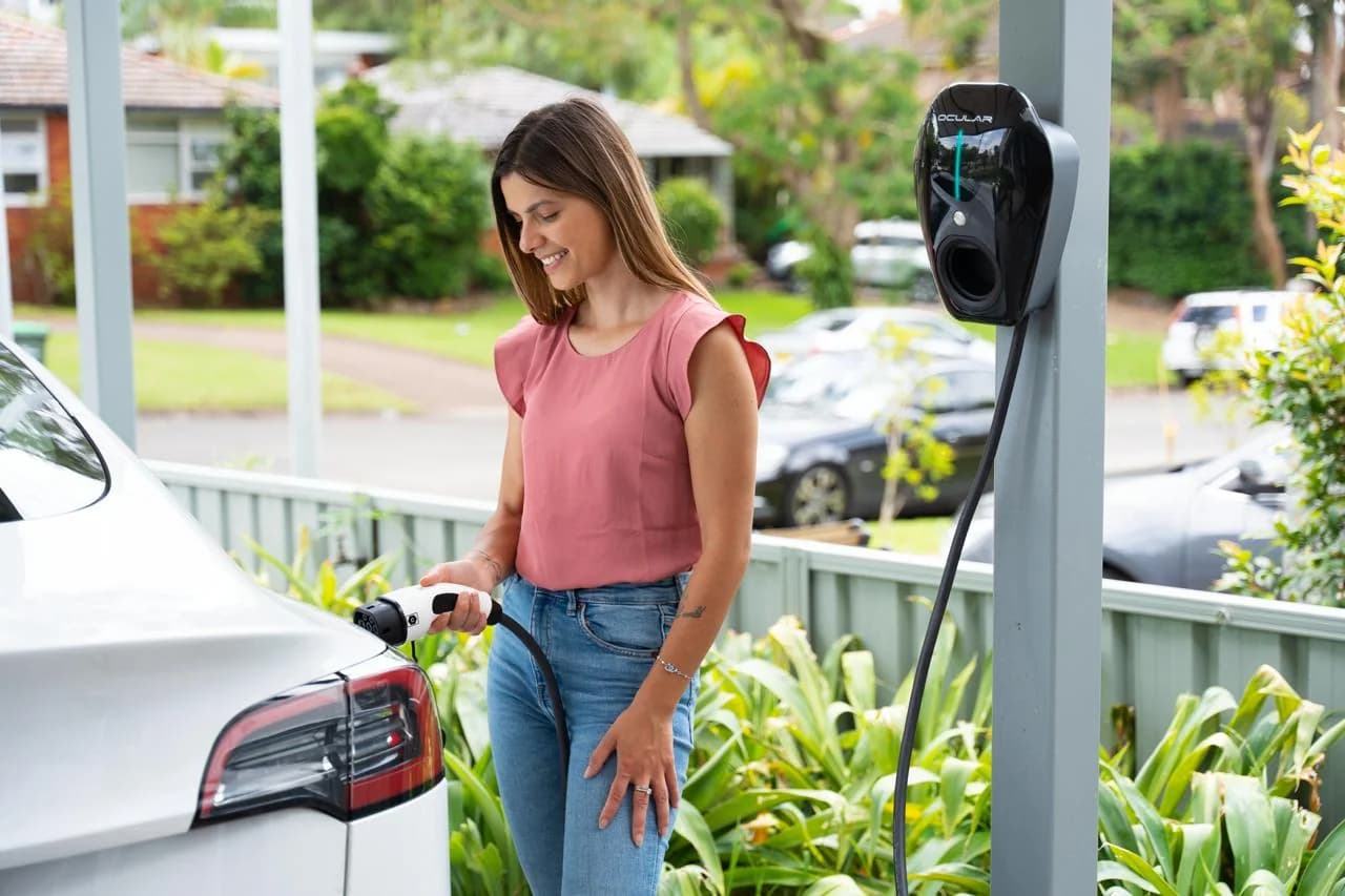 Woman plugging her electric car into an Ocular home EV charger mounted on a carport post